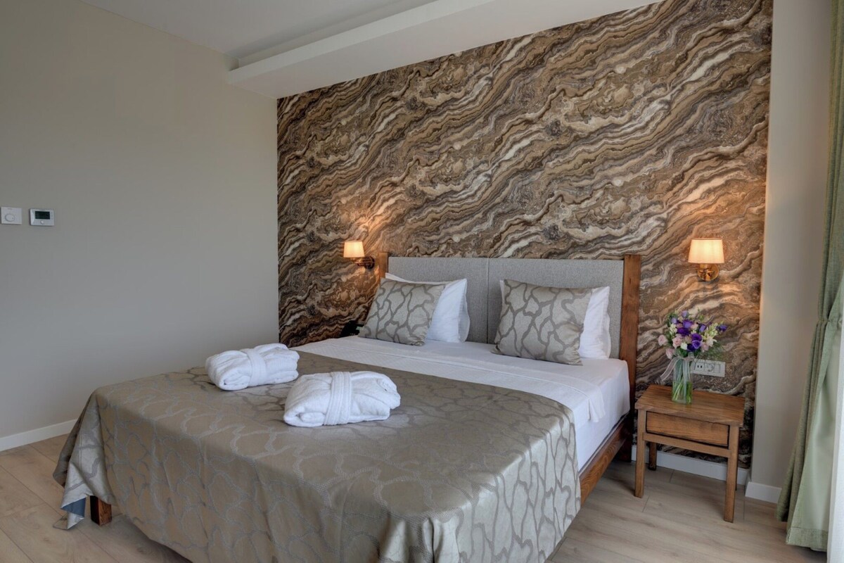 Una cama bien hecha con dos toallas, un papel tapiz con diseño de mármol y dos lámparas de noche.