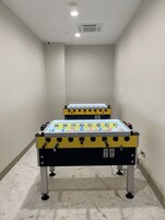 Dos mesas de fútbol de mesa en una habitación con paredes blancas y piso de mármol.