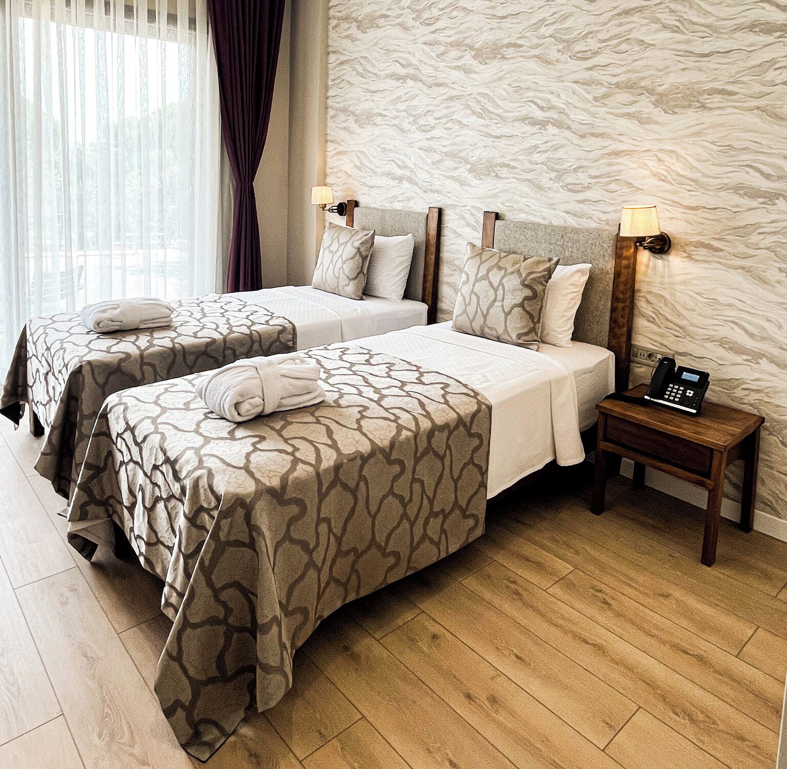 Habitación de hotel con dos camas, piso de madera, pared de piedra y mesita de noche con teléfono.