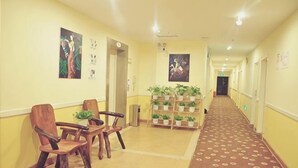 A hotel lobby with a carpeted floor, wooden chairs, a plant display, and a reception desk. - Jiahe Hotel (Xishuangbanna Jinghong Manting Park Poshui Plaza) (Jinghong)