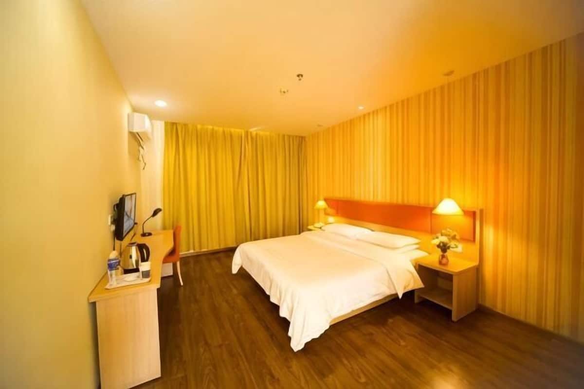 A hotel room with a bed, bedside table, lamp, and a desk with a chair.