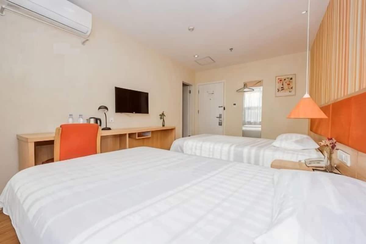 A hotel room with two beds, a desk, a TV, and a lamp.