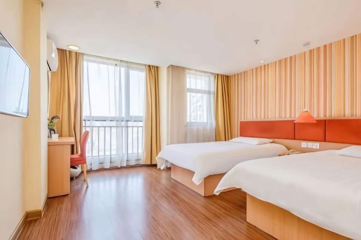 A hotel room with two beds, a desk, a chair, and a TV.
