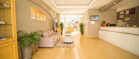 A hotel lobby with a reception desk, seating area, and a large potted plant.