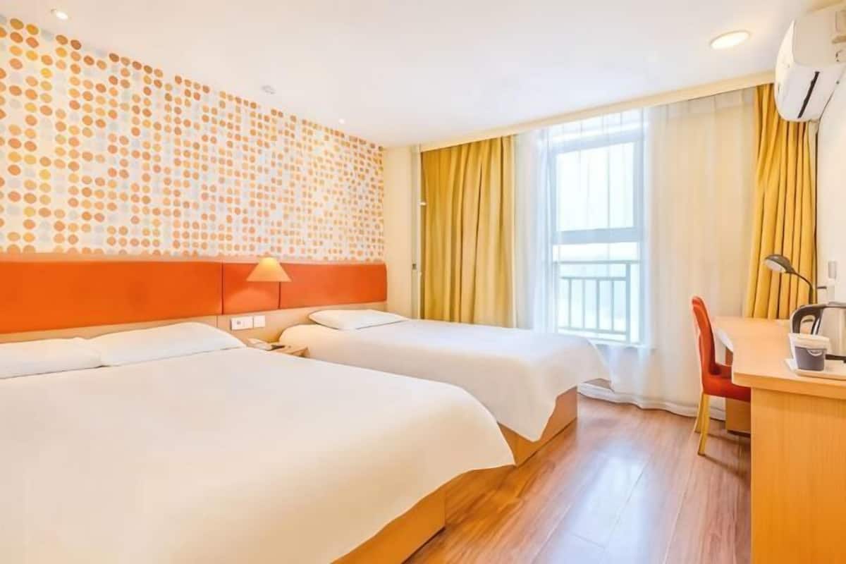 A hotel room with two beds, a desk, a chair, a window with curtains, and a wall with a patterned design.