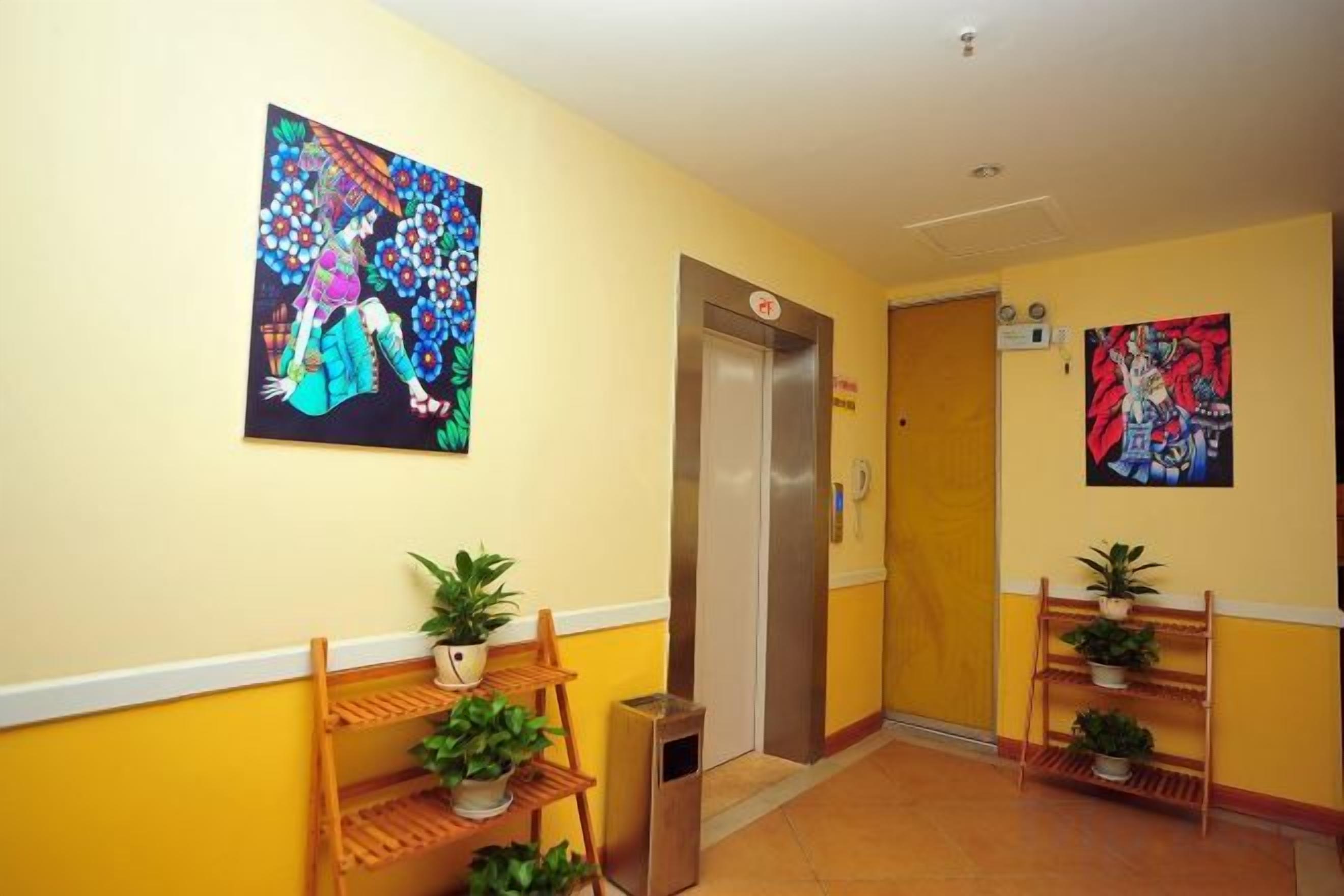 A hotel hallway with a wooden bench, potted plants, and two paintings on the walls.