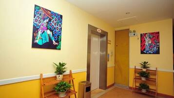 A hotel hallway with a wooden bench, potted plants, and two paintings on the walls.