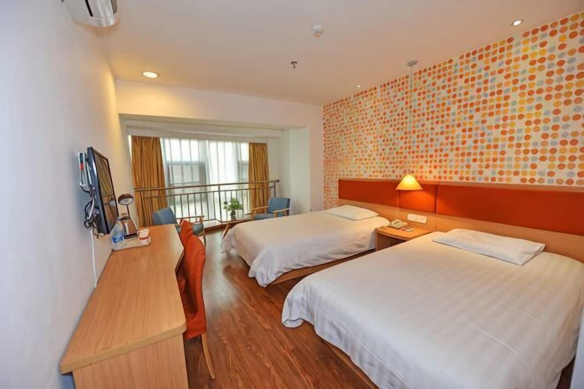 A hotel room with two beds, a desk, a chair, a window with curtains, and a patterned wall.