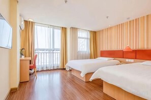 Ein Hotelzimmer mit zwei Betten, einem Schreibtisch, einem Sessel und einem Fernseher.