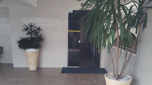 A spacious lobby with tiled flooring, two large potted plants, and a visible entrance to another area. - Apartment with swimming pool, garage, games room and elevator! (Aviação Praia Grande)