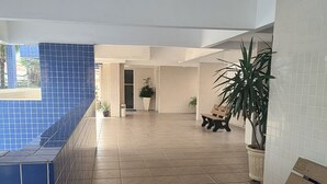 A spacious indoor area with a tiled floor, a bench, and potted plants. - Apartment with swimming pool, garage, games room and elevator! (Aviação Praia Grande)