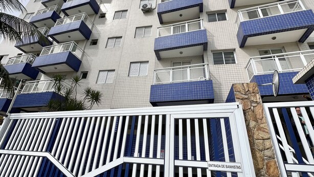 A multi-story residential building with balconies, a gated entrance, and a stone feature. - Apartment with swimming pool, garage, games room and elevator! (Aviação Praia Grande)