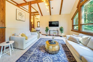 Relax in this spacious living room with a high ceiling and large window offering a view of the surrounding forest.