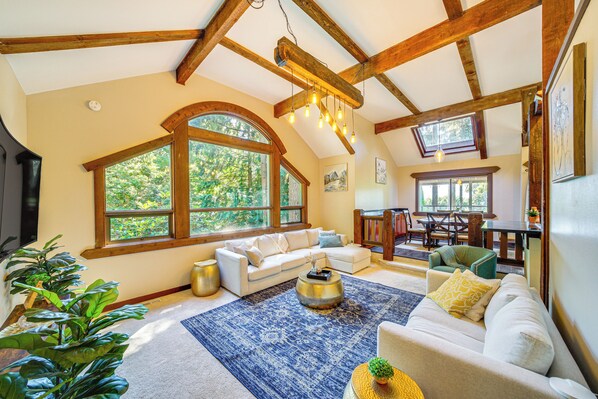 Relax in this spacious living area with high ceilings and a large arched window offering a view of lush greenery.