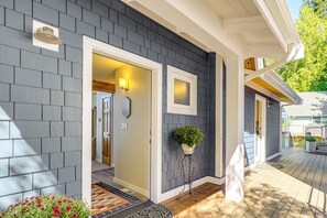 A house with a grey shingle exterior, a white door, and a small porch area with a potted plant. - Bayfront Home w/ Private Beach in Poulsbo! (Poulsbo)
