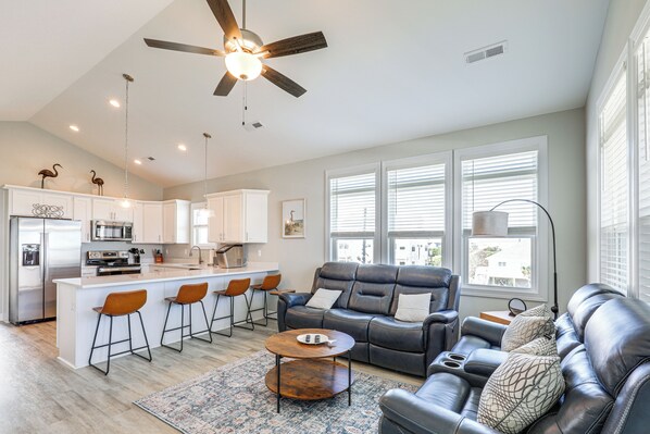 A modern kitchen with a central island, bar stools, a black leather sofa, and a patterned rug. - Walk to the Beach: North Topsail Beach Duplex (Sneads Ferry)