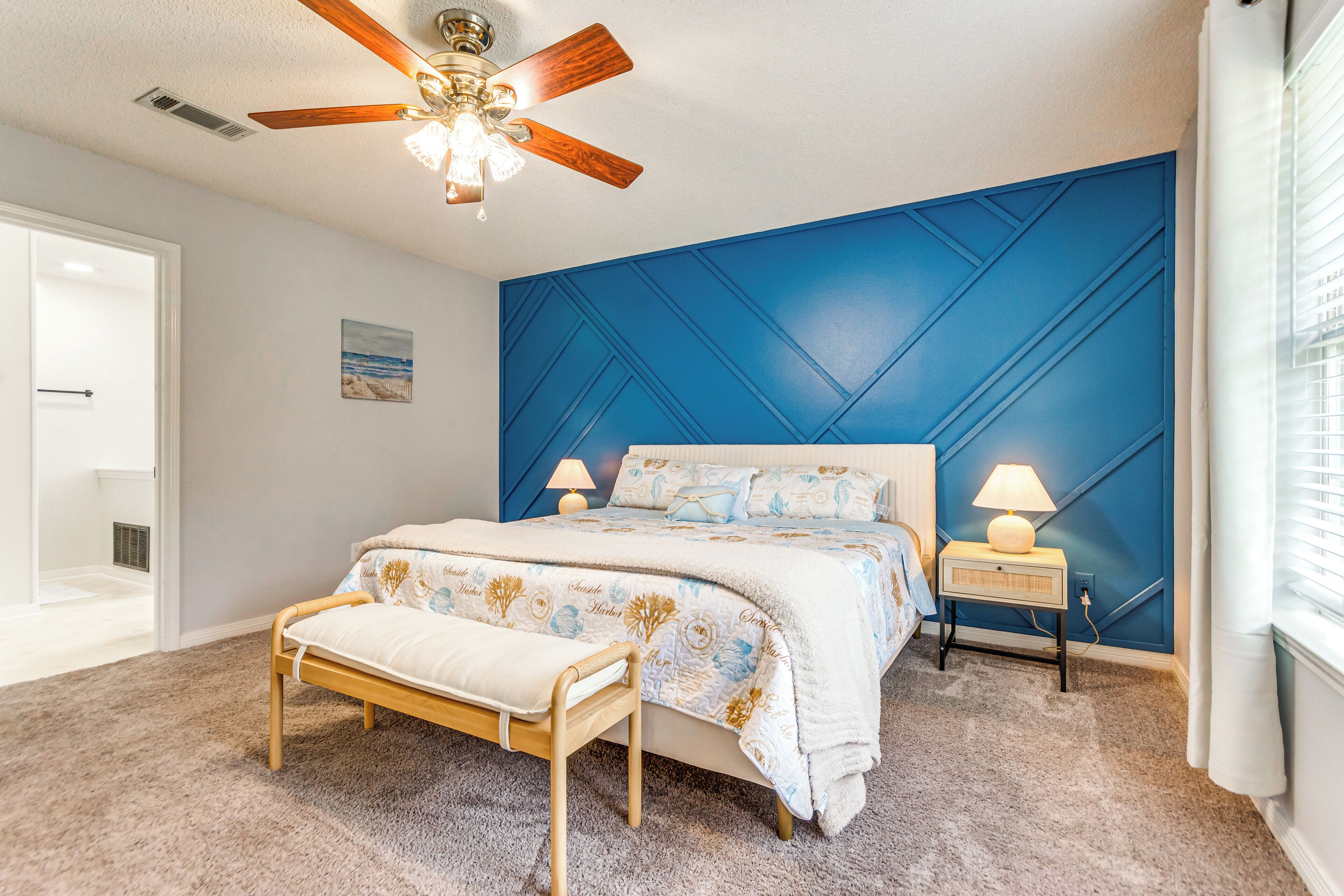 Een slaapkamer met een bed, nachtlampjes, een bankje, een plafondventilator en een blauwe accentmuur.