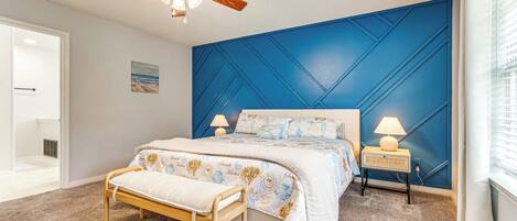 A bedroom with a bed, bedside lamps, a bench, a ceiling fan, and a blue accent wall.