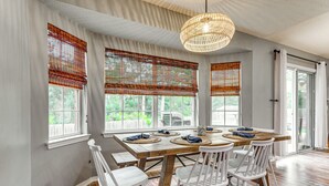 A dining area with a wooden table, white chairs, and a woven light fixture. - Pensacola Home w/ Fire Pit, 7 Mi to Beaches! (Pensacola)