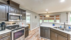 A modern kitchen with stainless steel appliances, wooden cabinets, and a large window with blinds. - Pensacola Home w/ Fire Pit, 7 Mi to Beaches! (Pensacola)