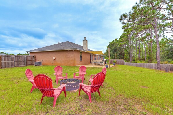 A backyard with a brick house, a fire pit, and red Adirondack chairs. - Pensacola Home w/ Fire Pit, 7 Mi to Beaches! (Pensacola)