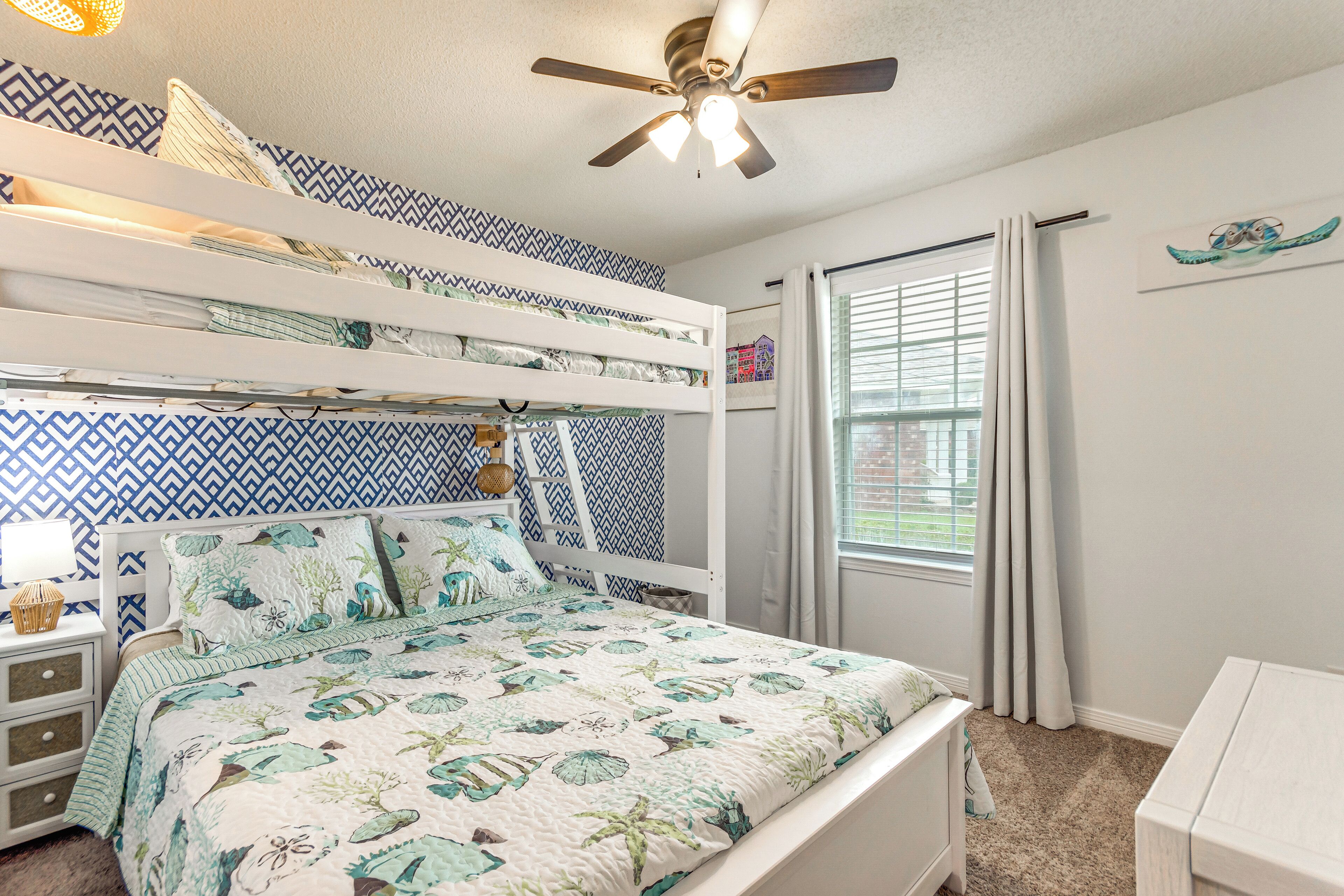 A bedroom with a bunk bed, a ceiling fan, a window with curtains, and a wall with a geometric pattern.