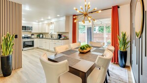 A modern kitchen with white cabinets, a dining area with a wooden table and chairs, and a large window with curtains. - Loveland Retreat Near Dtwn w/ Outdoor Dining! (Loveland)