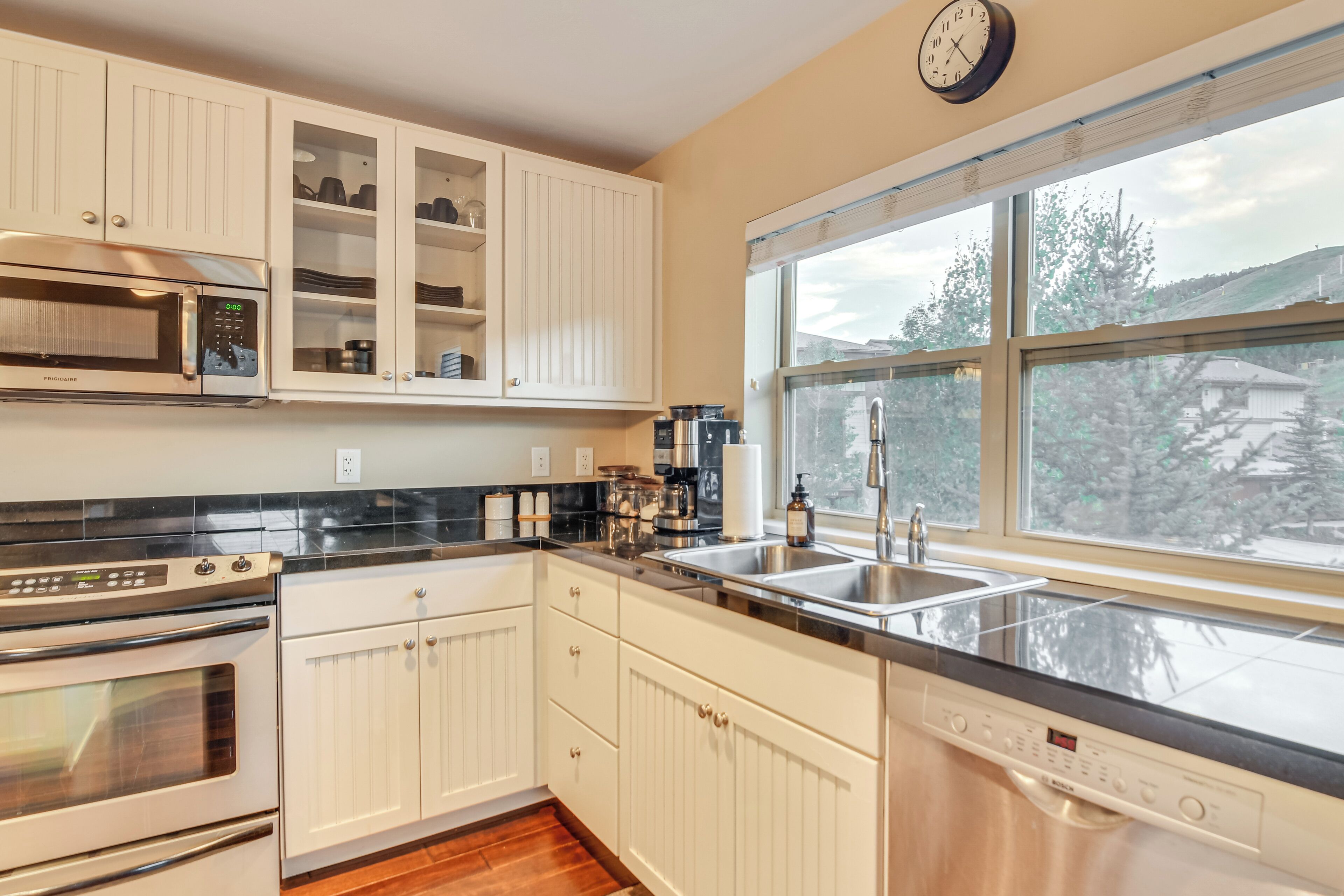 A modern kitchen with white cabinetry, stainless steel appliances, and a large window offering a view of the outdoors.