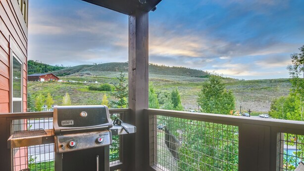 A balcony with a Weber grill and propane tank, overlooking a hilly landscape with a red building in the distance. - Ski-in/ski-out + Pool Access: Granby Ranch Gem (Granby)