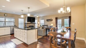 A modern kitchen with white cabinetry, a central island, and a dining area with wooden chairs and a table. - Ski-in/ski-out + Pool Access: Granby Ranch Gem (Granby)