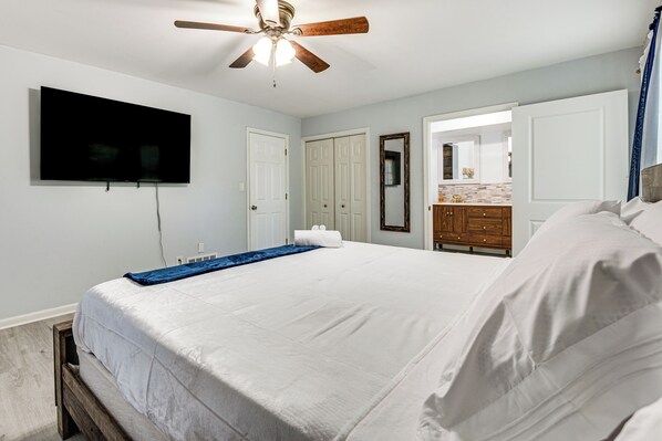 A bedroom with a bed, a ceiling fan, a TV, and a bathroom visible through an open door. - Spacious Home w/ Hot Tub, 14 Mi to Downtown Atl! (Atlanta)