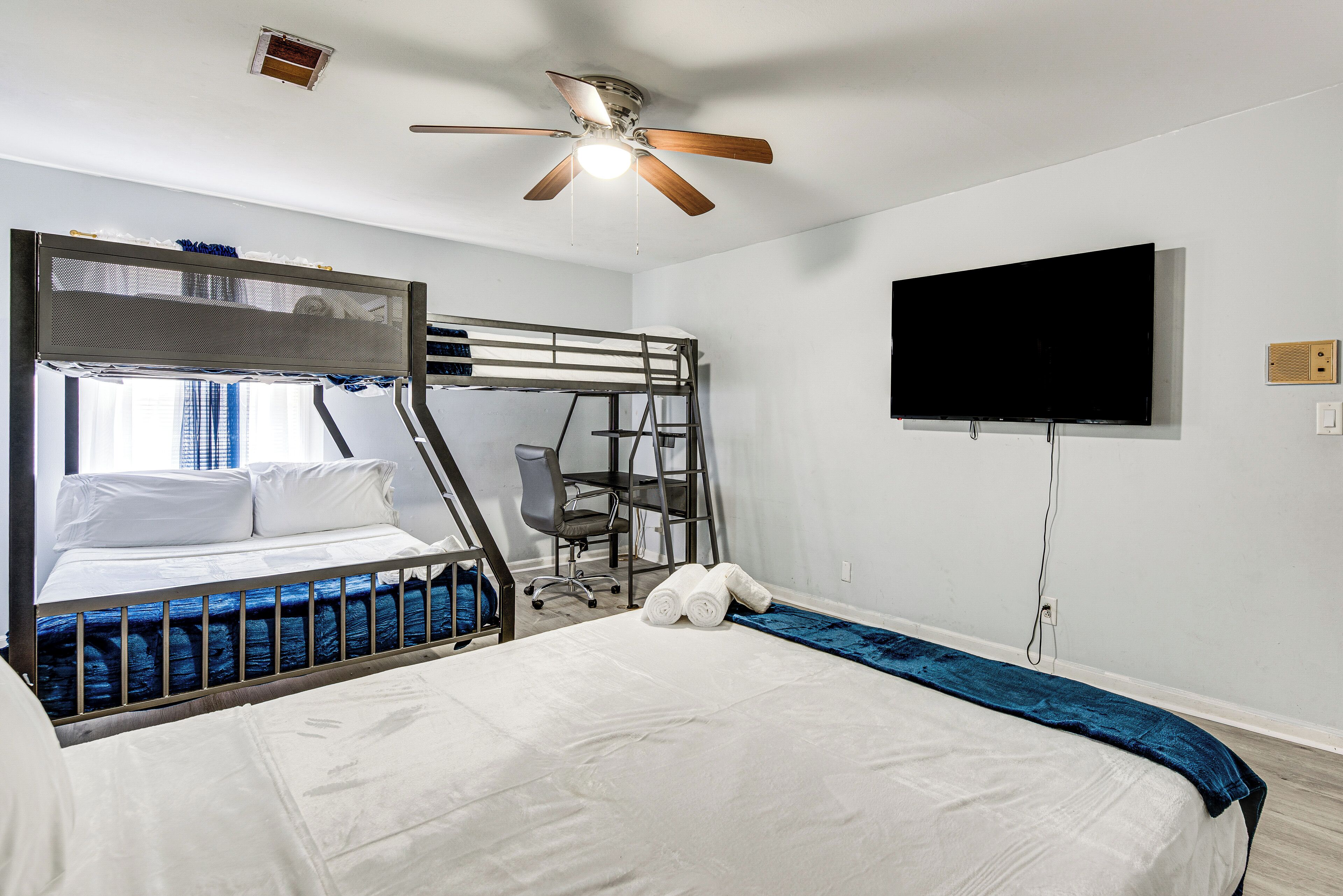 Ein Zimmer mit Etagenbetten, Deckenventilator, Flachbildfernseher und Schreibtisch mit Stuhl.