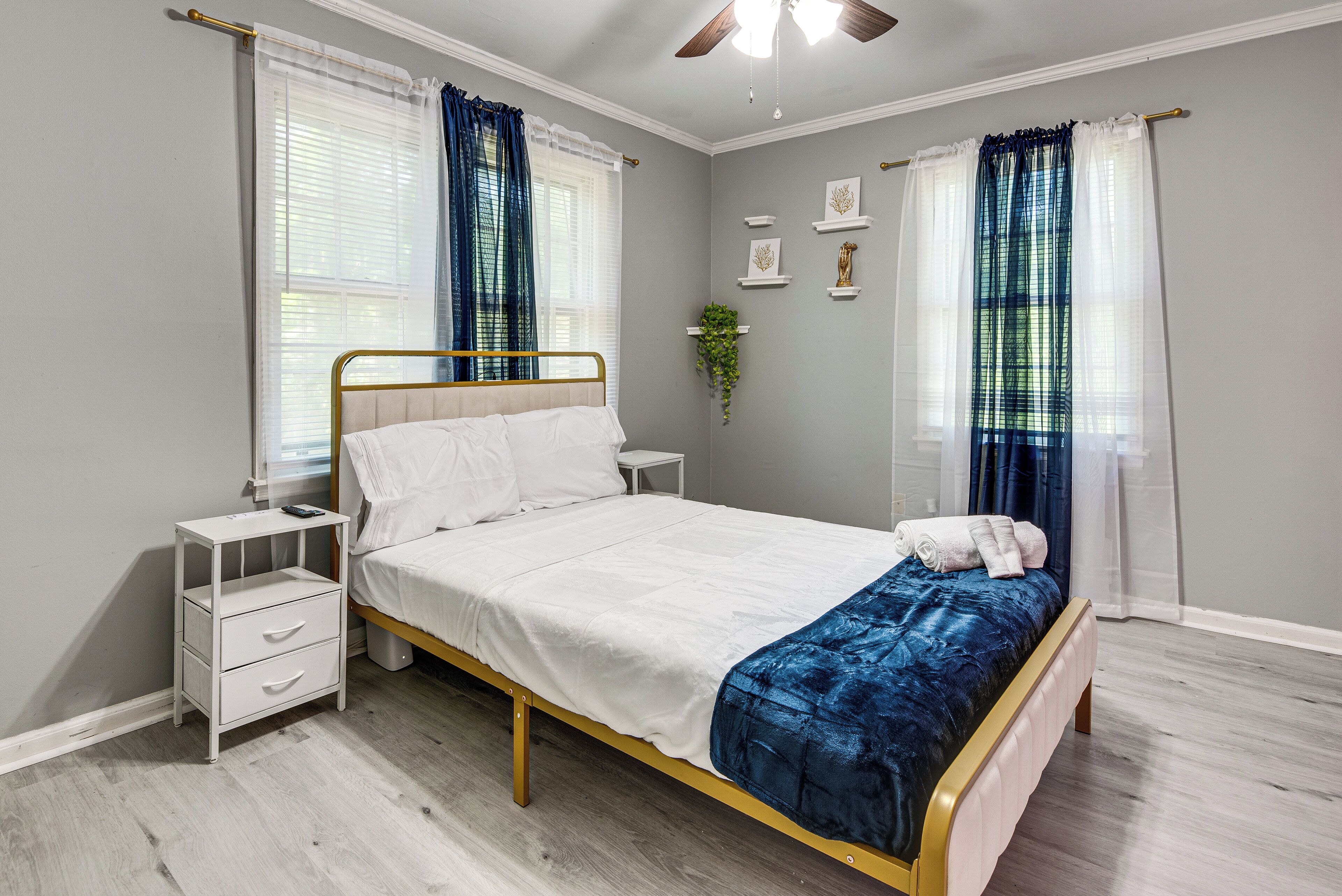 Ein Schlafzimmer mit Bett, Nachttischen, einem Fenster mit Vorhängen und einem Deckenventilator.