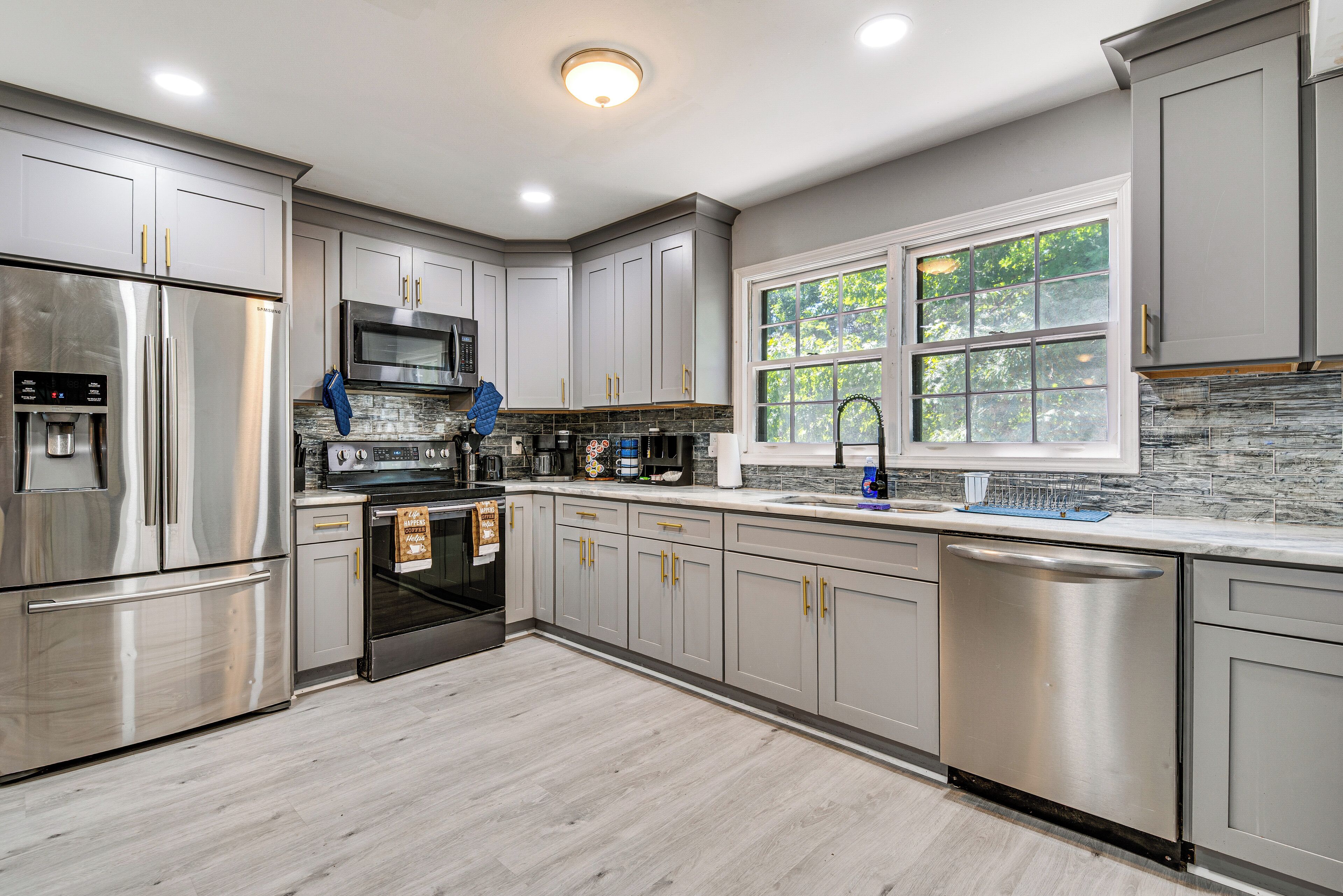 A modern kitchen with stainless steel appliances, grey cabinetry, and a large window with a view of trees.