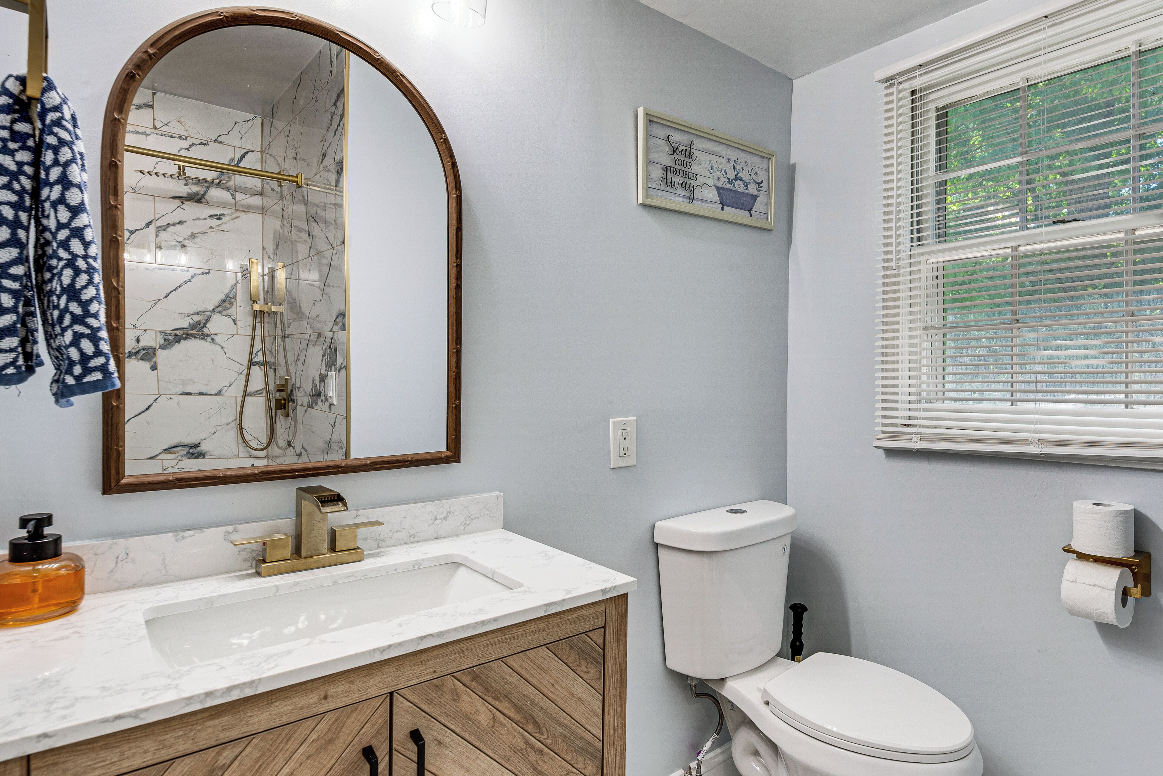 A bathroom with a marble sink, wooden cabinet, toilet, and a mirror with a gold frame.