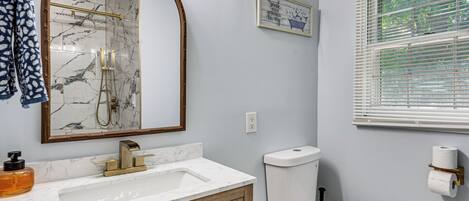 A bathroom with a marble sink, wooden cabinet, toilet, and a mirror with a gold frame.