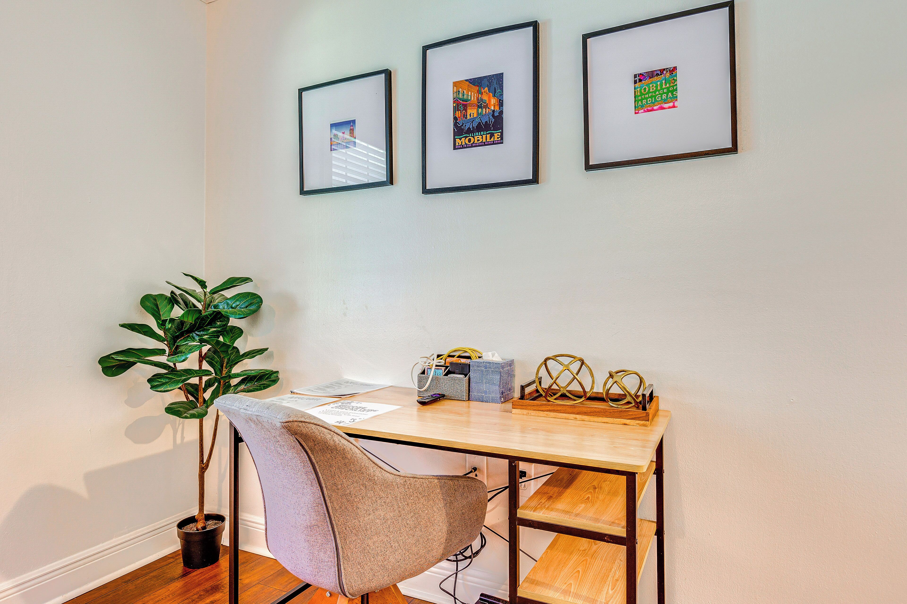 A workspace with a desk, chair, framed pictures, a potted plant, and a small table with items.