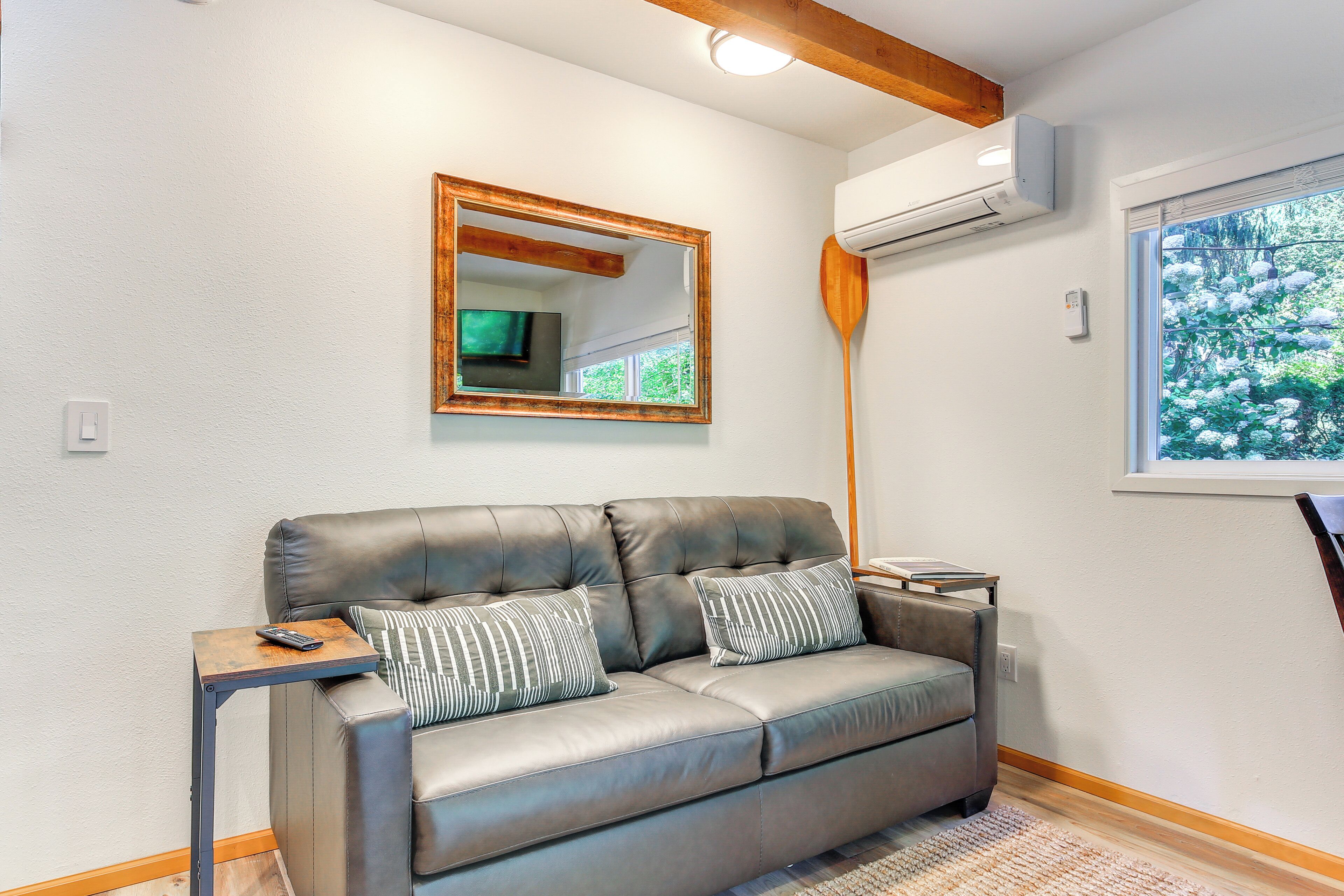 A modern living room with a leather sofa, a wooden side table, a wooden paddle, and a large window with a view of trees.