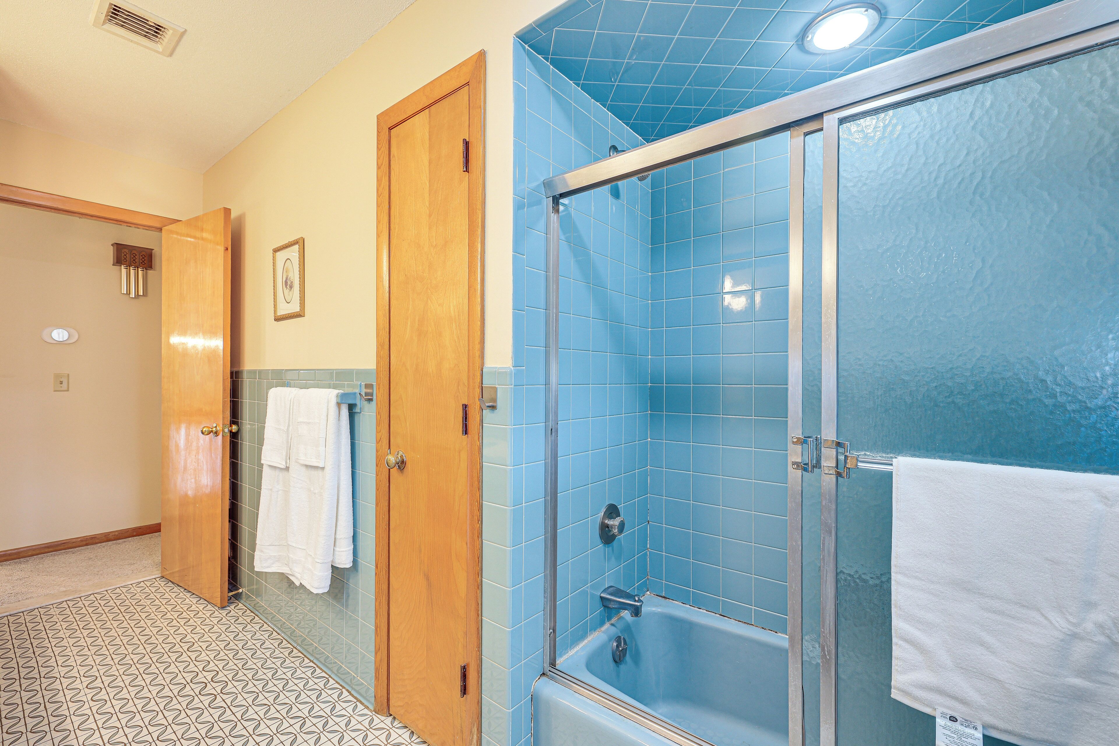 A bathroom with a glass-enclosed shower, a wooden door, and a patterned floor.