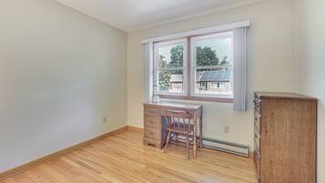 Una habitación con piso de madera, un escritorio de madera con cajones, una silla y un armario de madera.