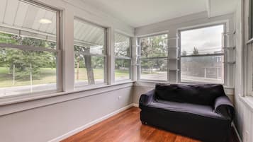Una habitación con ventanas amplias, piso de madera y un sofá negro.