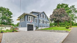 A two-story house with a garage, a front yard with a lawn, and a large tree. - Madison Home w/ Patio: Walk to Main Street! (Madison)