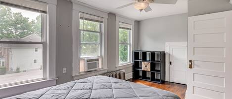 A bedroom with a large bed, a ceiling fan, and a view of the outside.