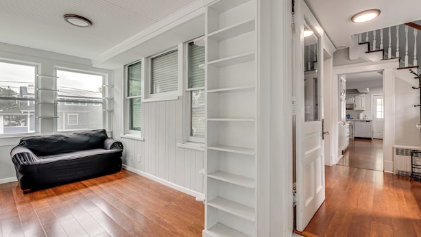 A spacious living room with hardwood floors, a black leather sofa, and a white shelving unit. - Madison Home w/ Patio: Walk to Main Street! (Madison)