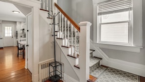 A staircase with white railings and wooden steps, leading to a room with a patterned floor and a window with blinds. - Madison Home w/ Patio: Walk to Main Street! (Madison)