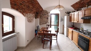 A kitchen with a dining table, chairs, a hanging light fixture, and wooden cabinets. - Apartment in historic township (Boissano)
