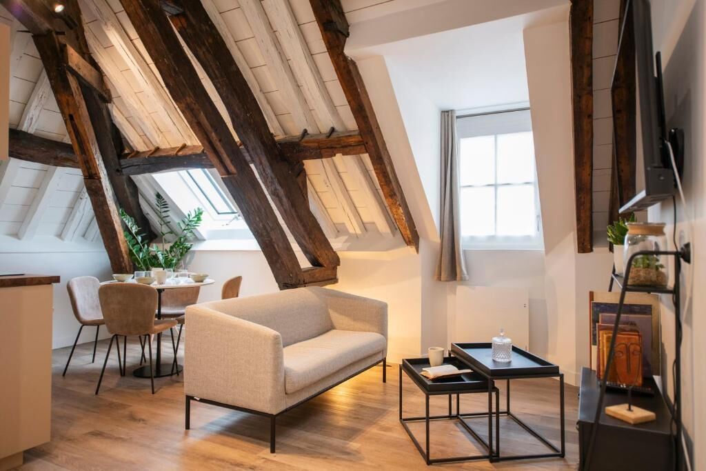 A cozy loft-style room with a high ceiling, exposed wooden beams, a sofa, a dining table with chairs, and a small coffee table.