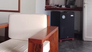 Een kamer met een witte bank, een klein houten tafeltje, een koelkast en een witte deur.