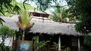 Een gebouw met rieten dak en een bord waarop staat: 'LES BOUCANIERES HOTEL'.