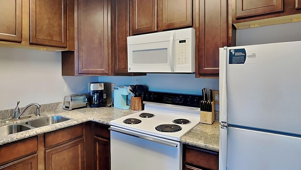 A kitchen with wooden cabinets, a white stove, a microwave, a toaster, and a refrigerator. - 1BD/1BA Condo w. Hall Bunk Bed, Steps from Beach, Pool + Hot Tub (Perdido Key)